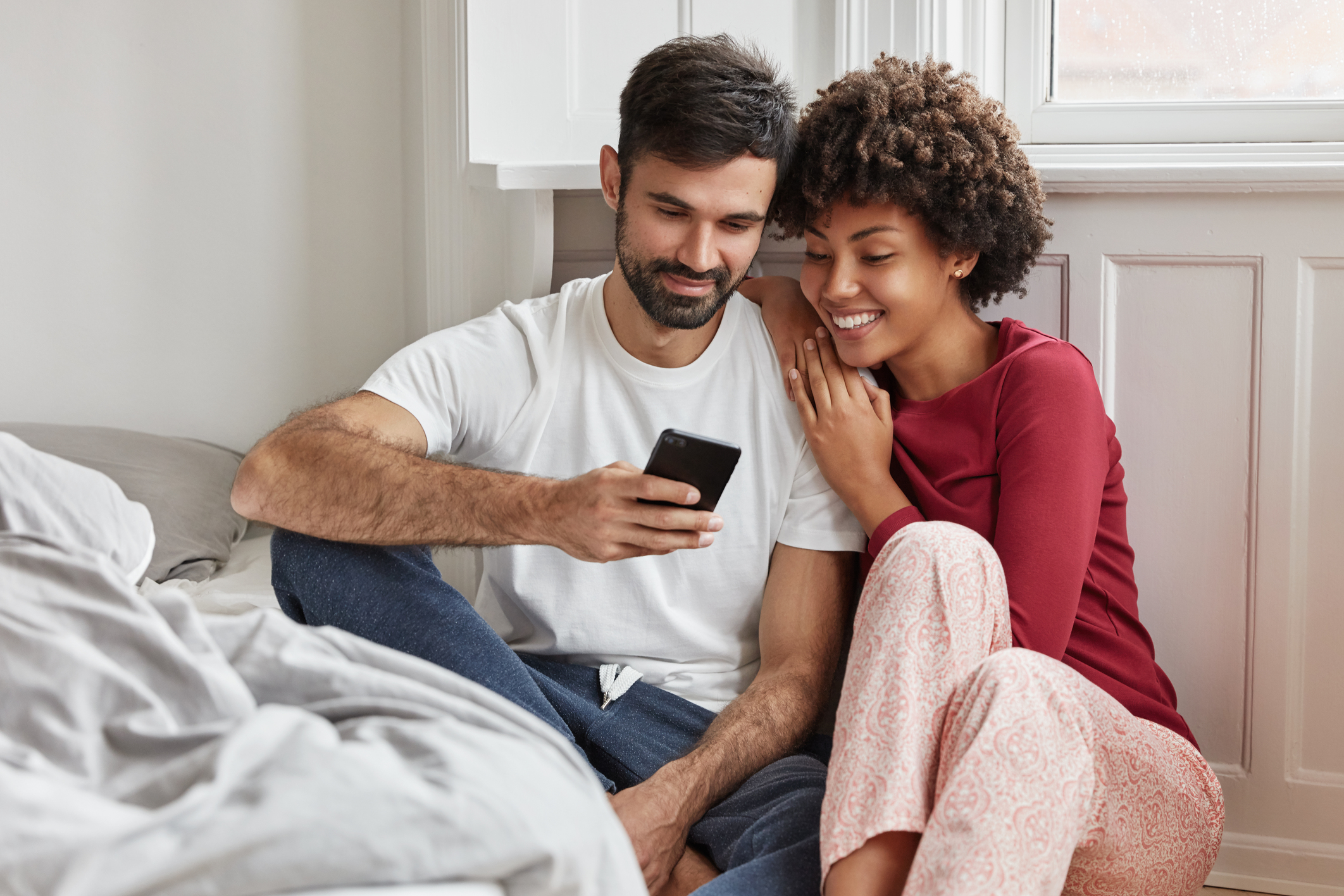 Adorable couple sitting on the floor near the bed and enjoying their domestic environment